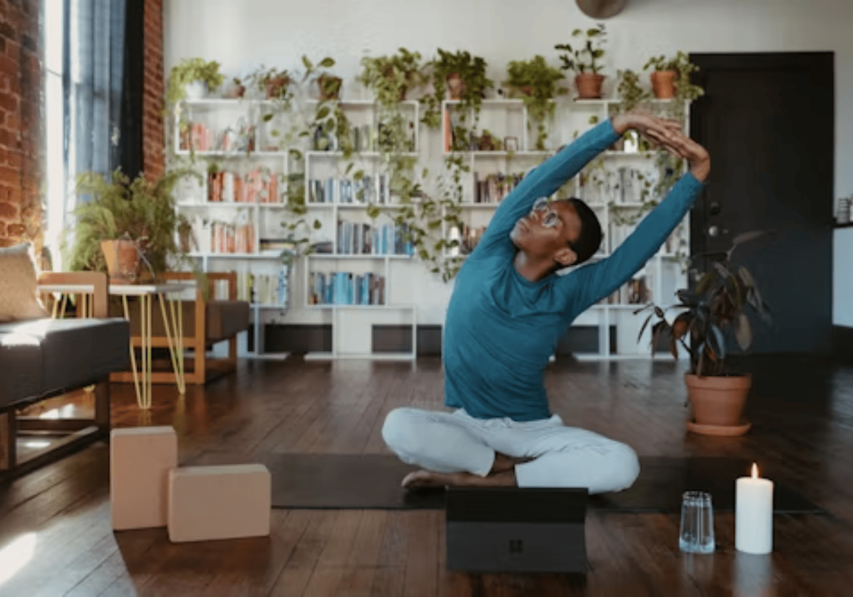 Person doing a seated yoga stretch in a bright room with plants and shelves in the background