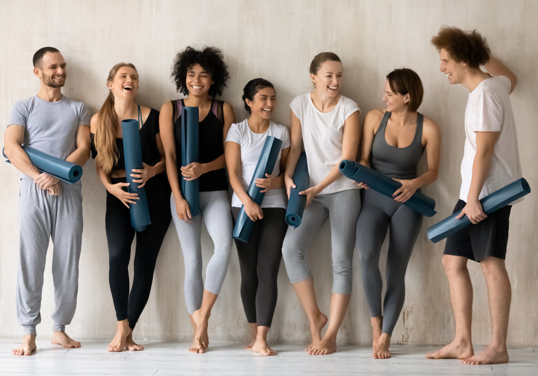 Group of people in workout clothes holding yoga mats, smiling in a bright studio
