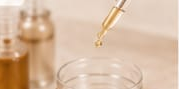 Contagocce che eroga liquido in un piccolo vasetto di vetro su una superficie beige