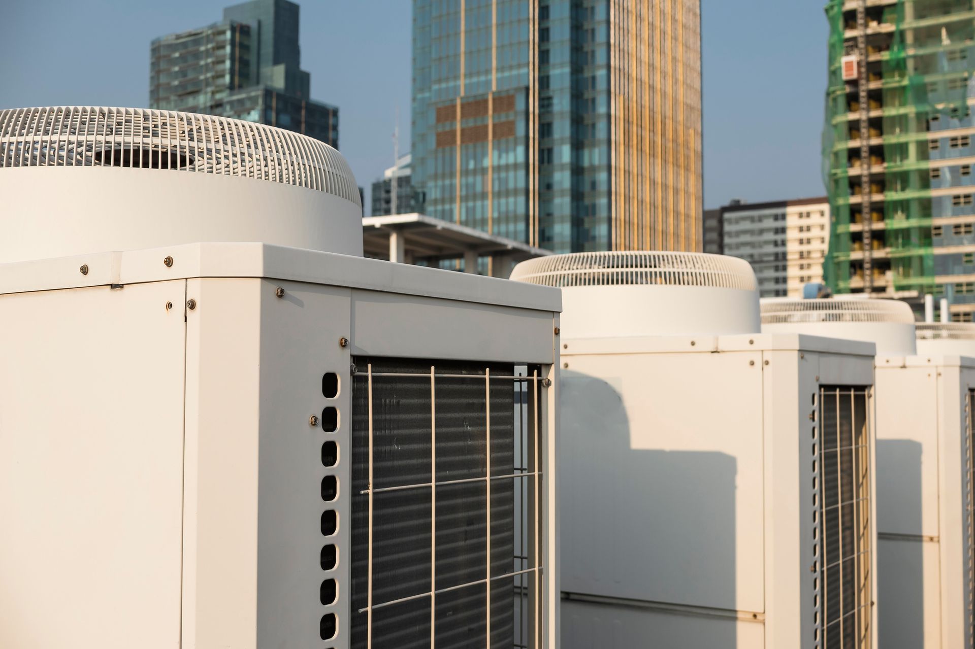 Rooftop HVAC units and air conditioning condensers on urban building with modern skyline background.