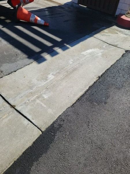 Sidewalk curb ramp with orange traffic cones and painted shadows beside a street.