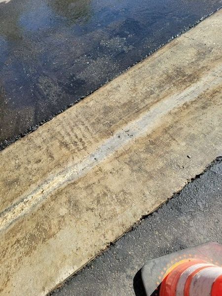 Wet curb beside dark pavement, with an orange traffic cone partially visible at the bottom right.