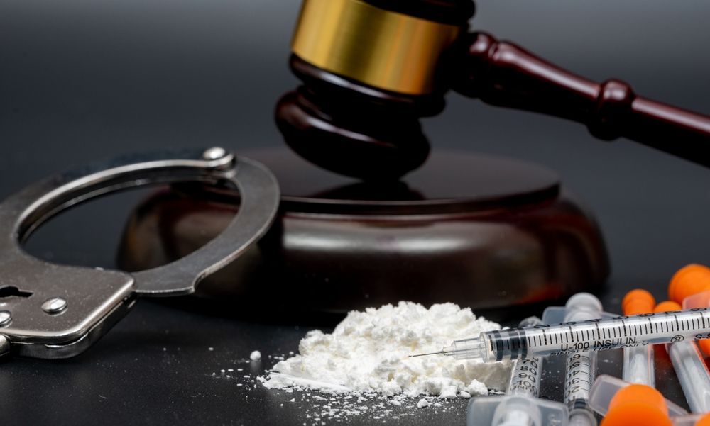 Handcuffs, gavel, and drugs (powder and syringes) on a dark surface, symbolizing crime and the legal system.