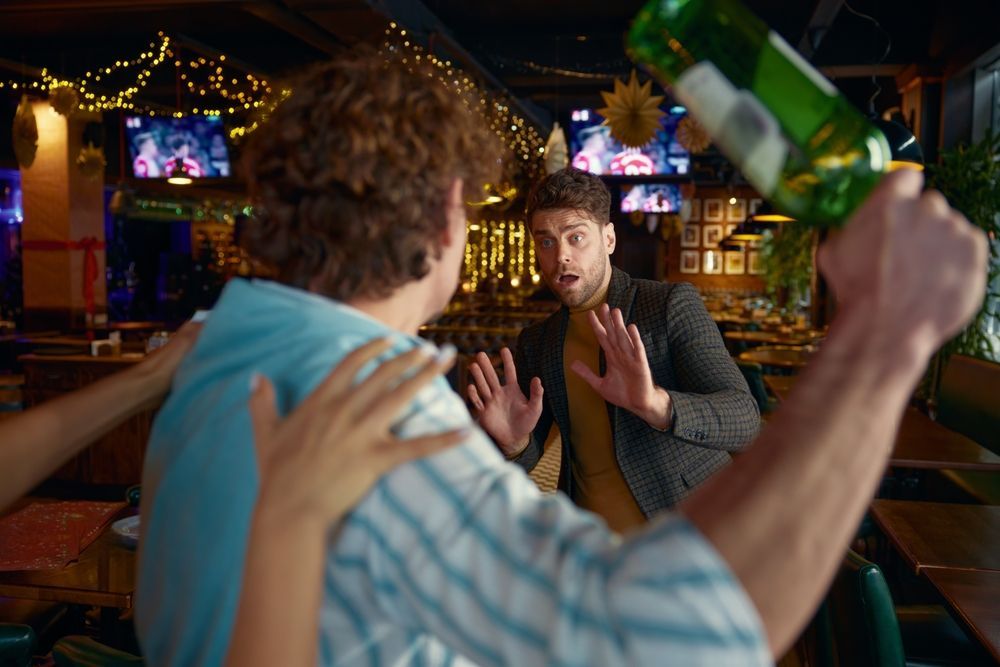 Man about to throw a beer bottle at another man in a bar. A third person is holding the thrower back.
