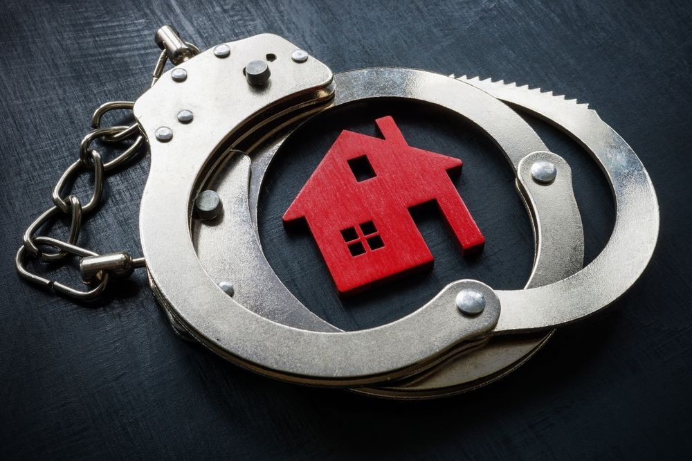 Handcuffs encircle a small red house, on a dark surface.