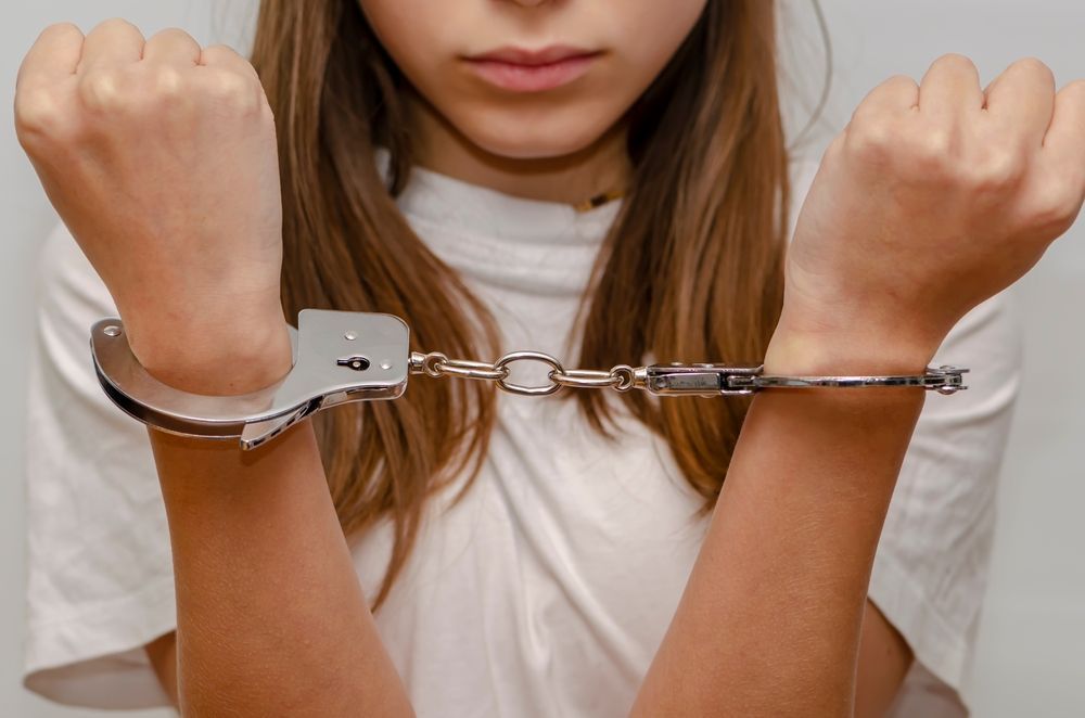 Hands cuffed in front of a person wearing a white shirt.
