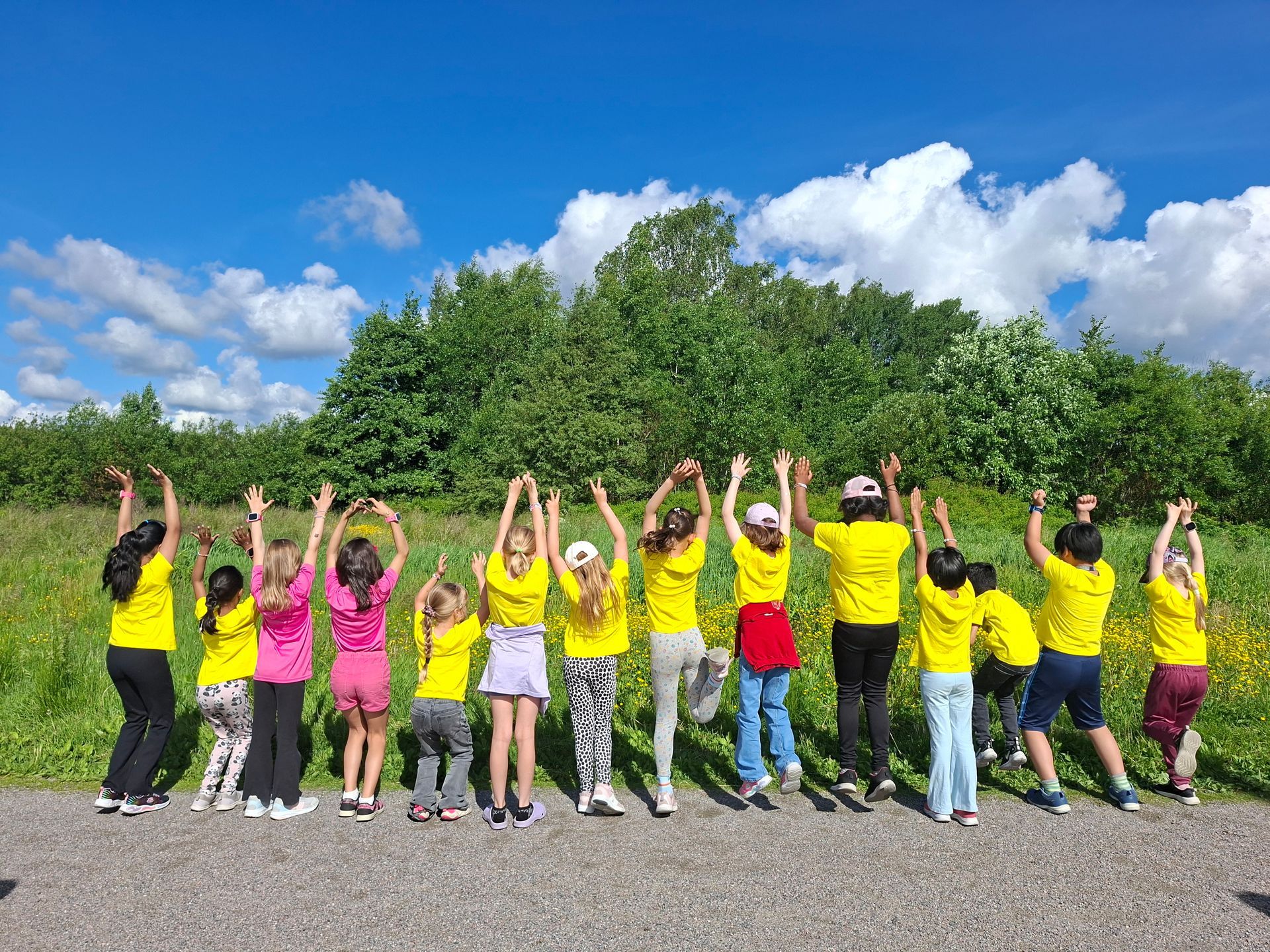 Group of children facing backwards in a field with hands raised in the air.