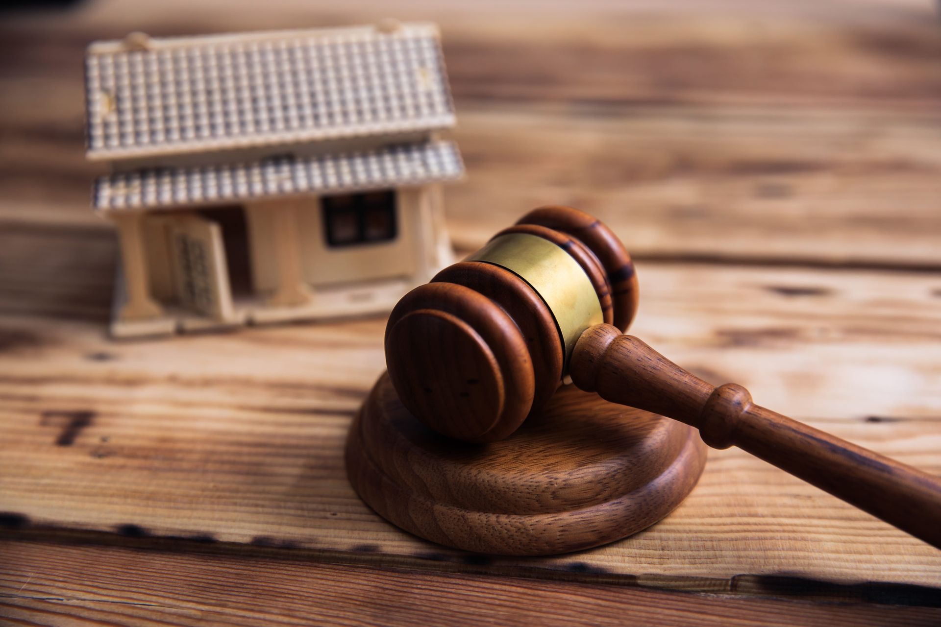 Judge’s gavel on a wooden table beside a small house model, symbolizing property law or foreclosure.