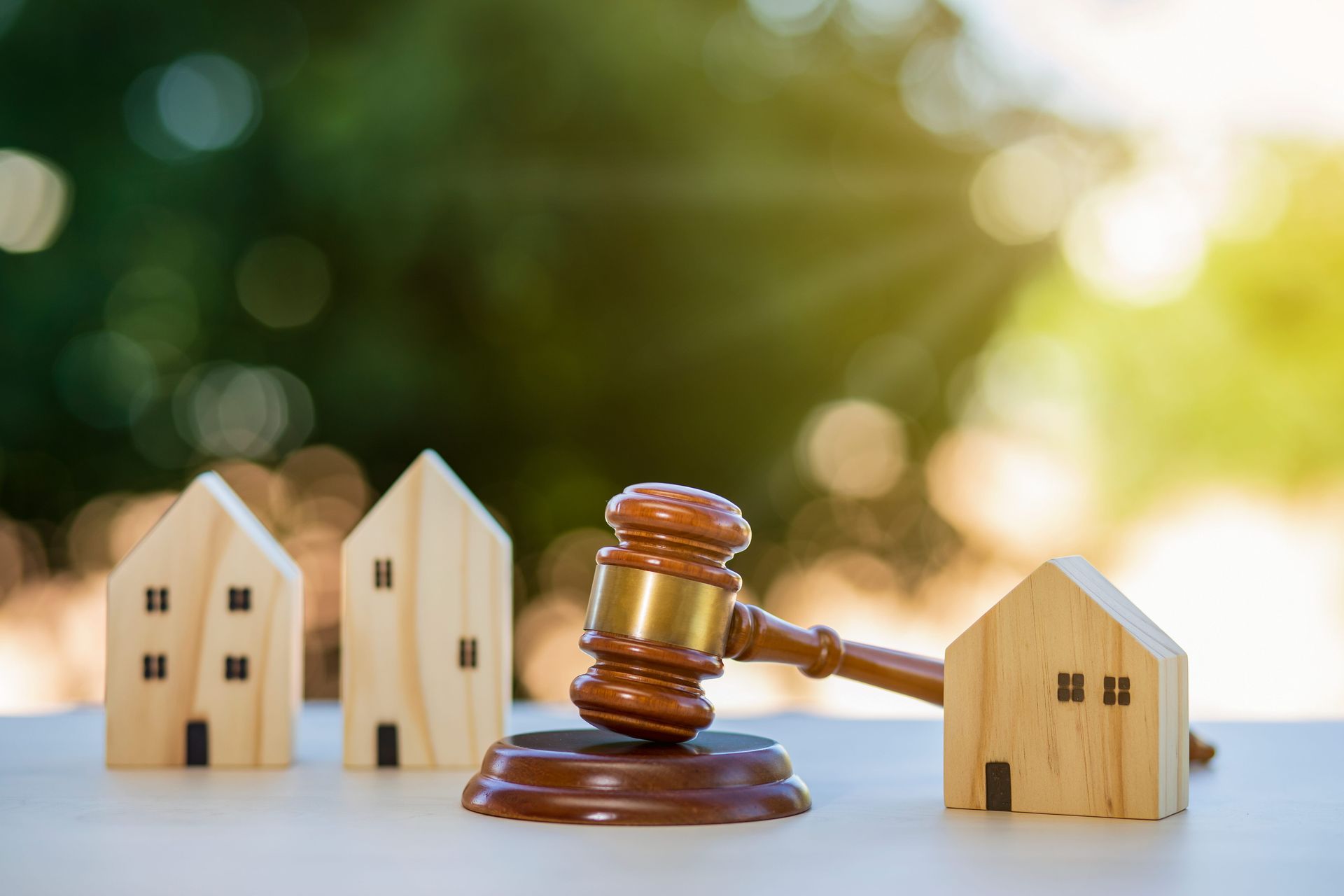 Wooden gavel striking a miniature house, other houses in the background, bokeh effect.