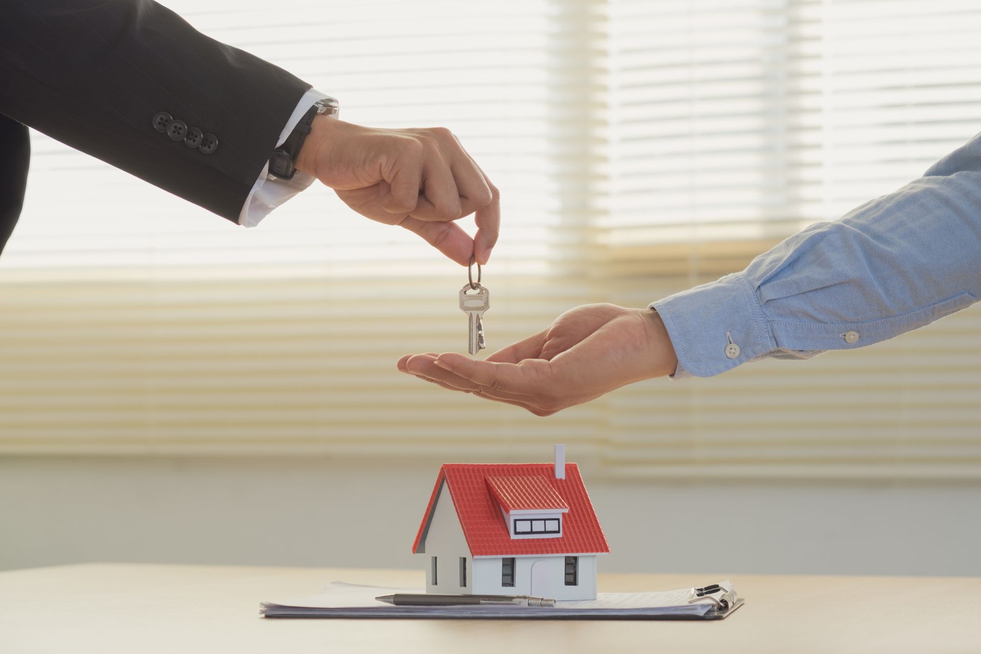 Handing over house key over small house model on a table.