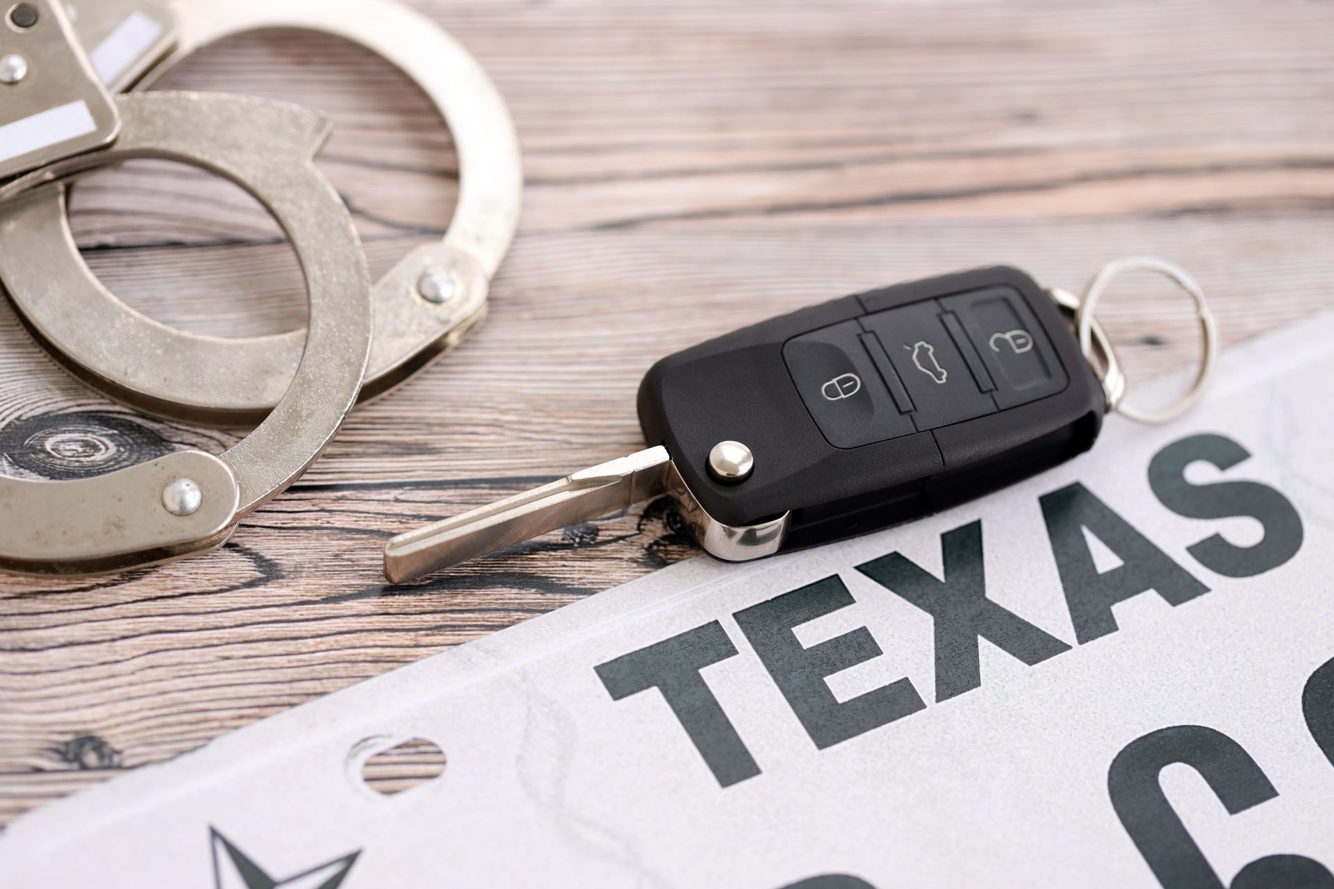 Handcuffs, car keys, and Texas license plate on wooden surface.