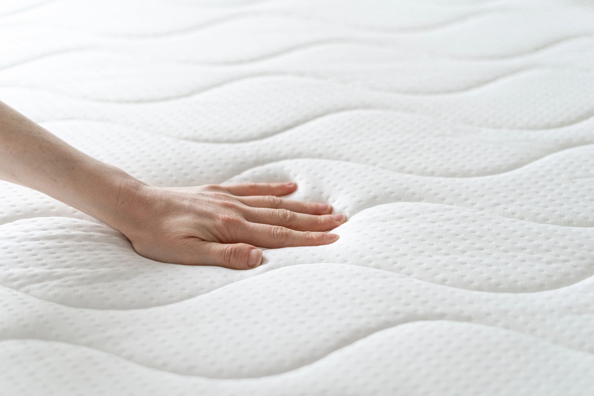 La mano di una persona preme su un morbido materasso bianco, a dimostrazione della sua consistenza e del suo comfort.