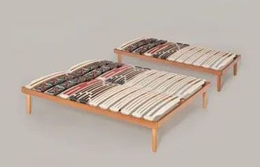 Due telai letto regolabili con gambe in legno e doghe decorate, su sfondo neutro.