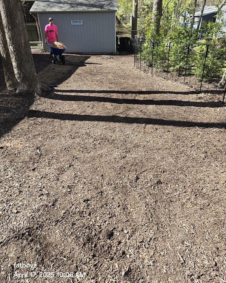 Person in a pink shirt standing beside a dog near a gray shed in a wooded yard