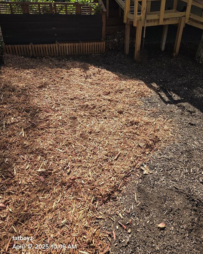 Mulched yard beside a wooden deck, with a dark soil or gravel path along the right side.