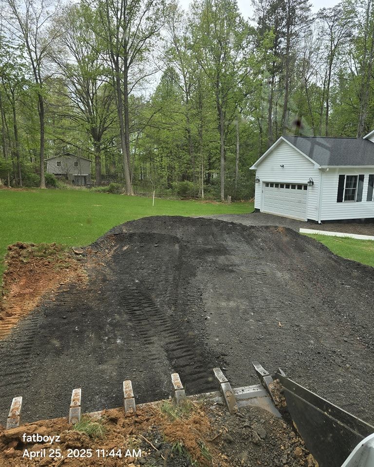 Gravel driveway under construction beside a white garage, with trees and a green yard nearby.
