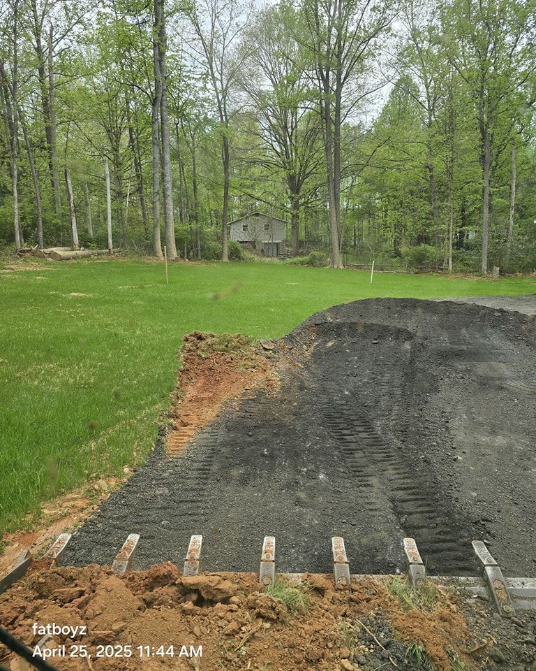 Gravel driveway edge with wooden stakes beside a grassy yard and trees in the background