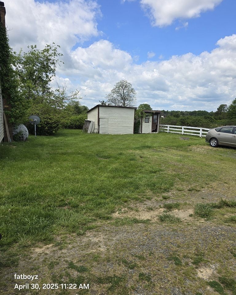 Grassy yard with small shed, white fence, parked car, and cloudy sky