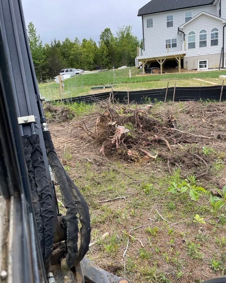 Cleared backyard with tree stump and uprooted brush near a white house under construction