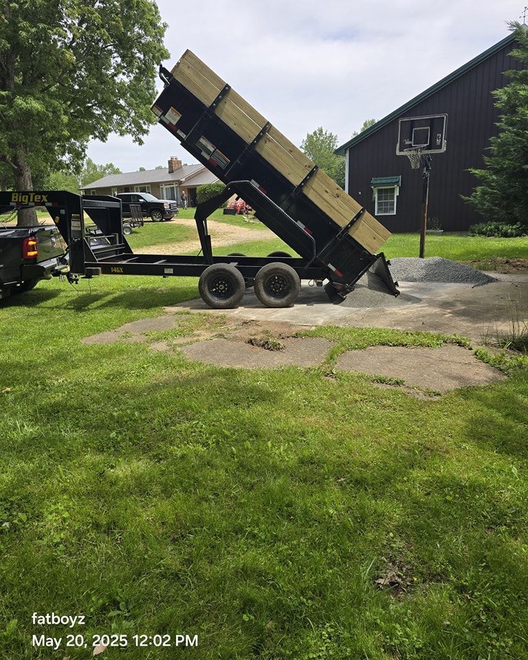 Dump trailer tilted up on a trailer in a grassy yard near a dark house.