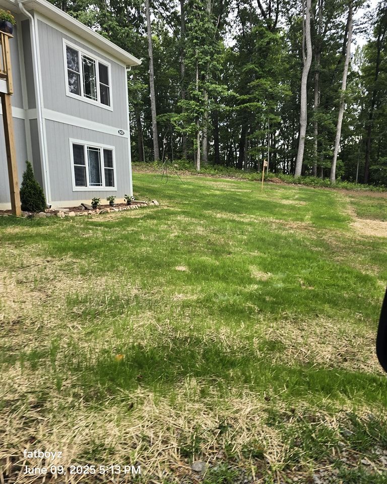 Side of a gray house beside a patchy green lawn and wooded backyard.