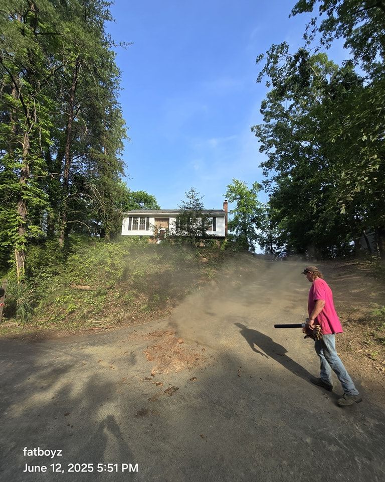 Person in a pink shirt walking on a dusty hill toward a house under trees.