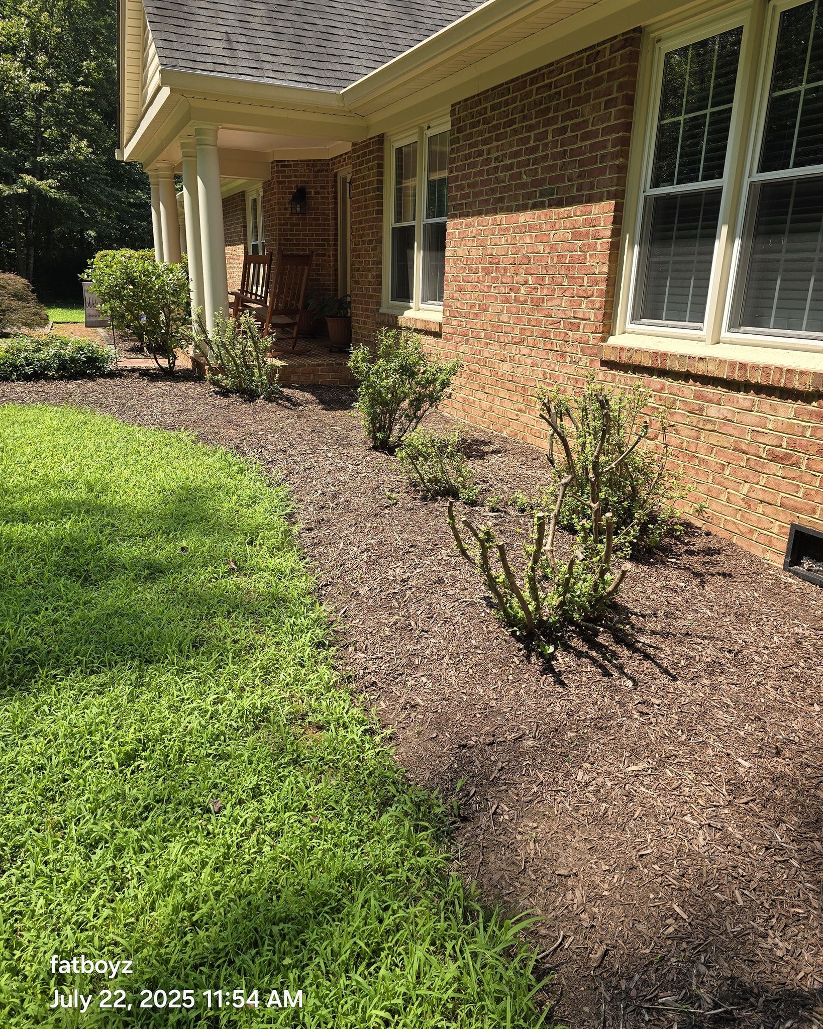 Brick house exterior with green lawn, mulch beds, shrubs, and a covered front porch