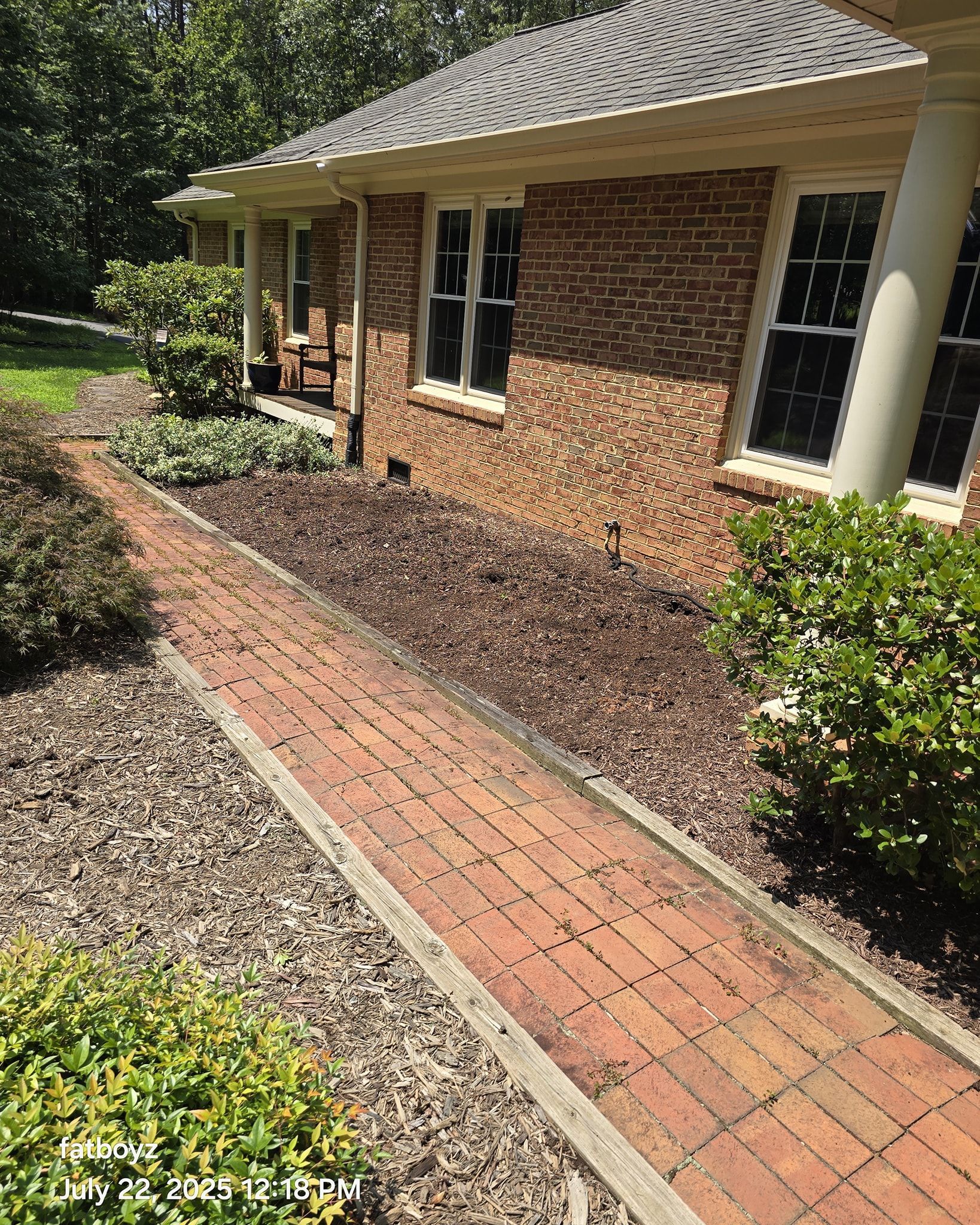 Brick house with a red brick walkway and landscaped garden beds along the side.