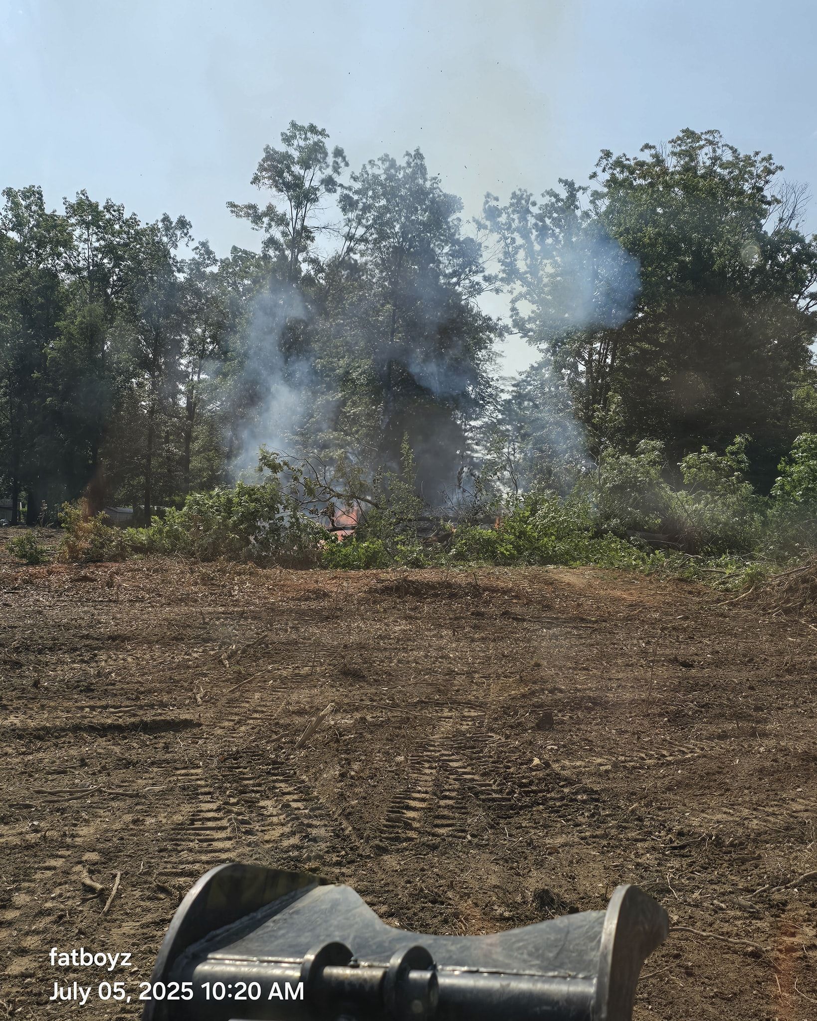 Person lying on dry ground near smoky brush in a wooded area