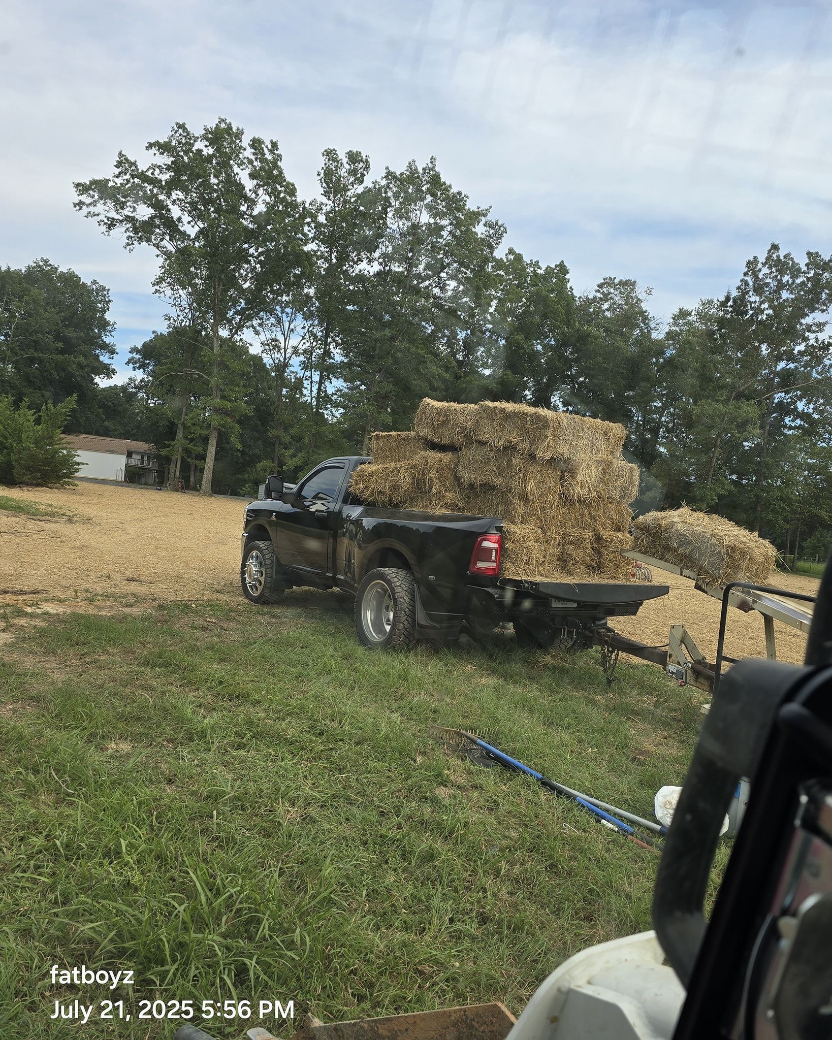 ATV hauling a trailer piled high with hay in a grassy field near trees and a dirt pile