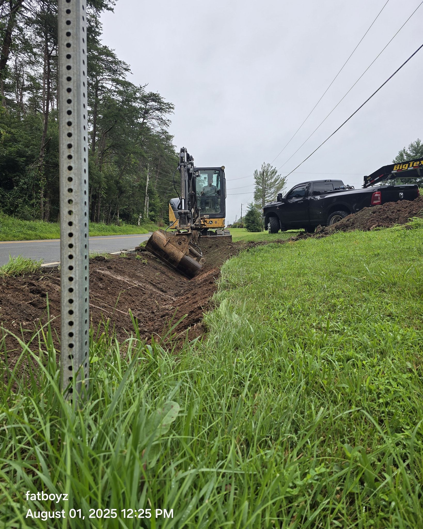 Roadside ditch excavation with an excavator and dump truck beside a wet rural road.