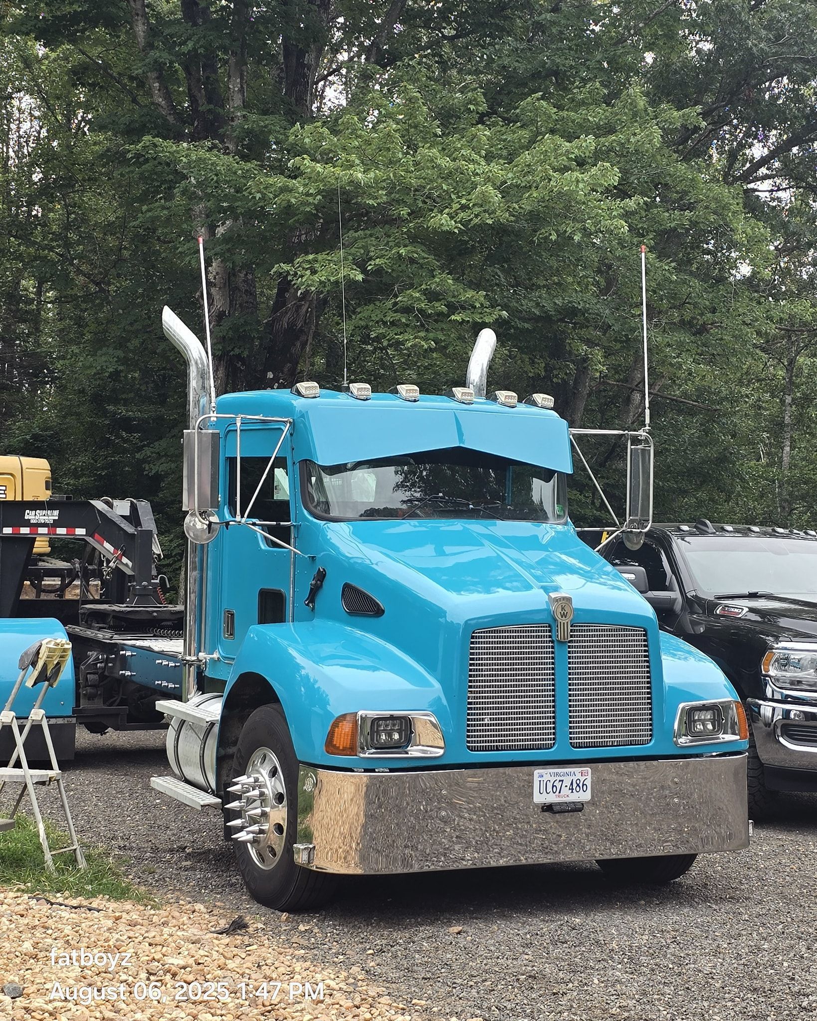 Blue semi-truck parked outdoors among other vehicles on a tree-lined street