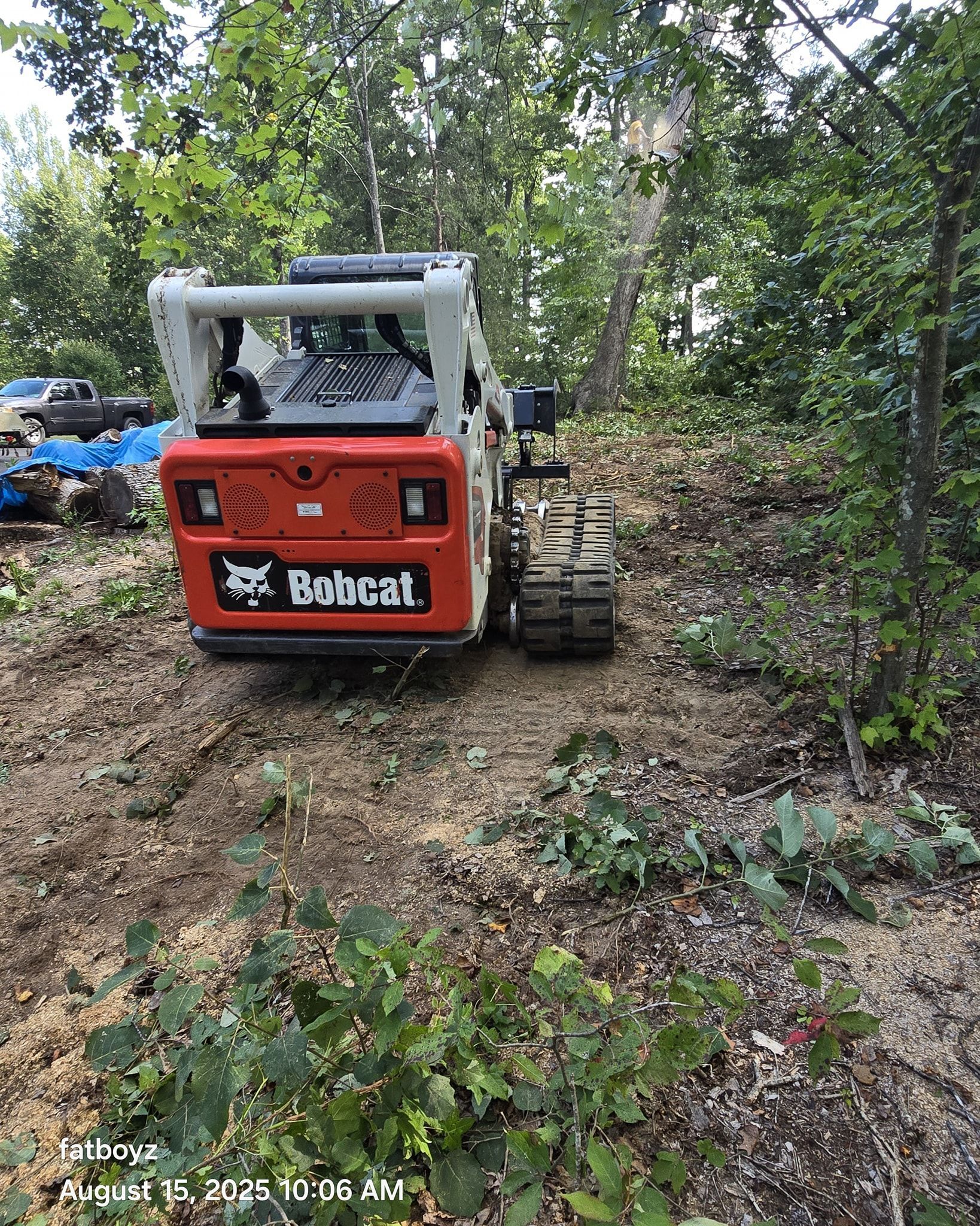 Orange Bobcat skid steer on a wooded dirt trail, viewed from behind.