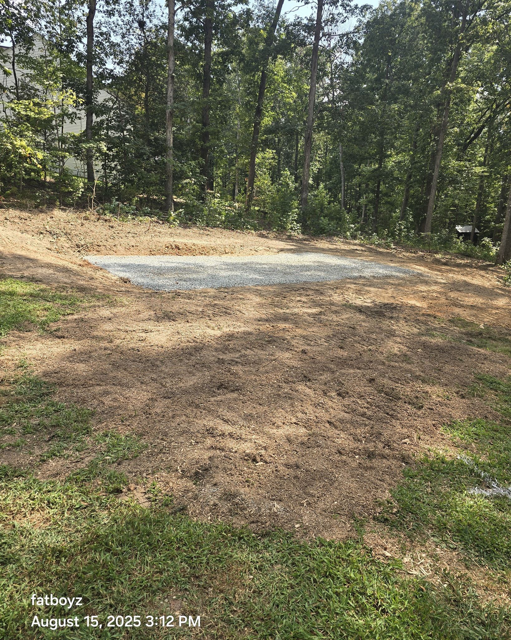 Wooded outdoor clearing with a gravel patch on the ground and trees in the background