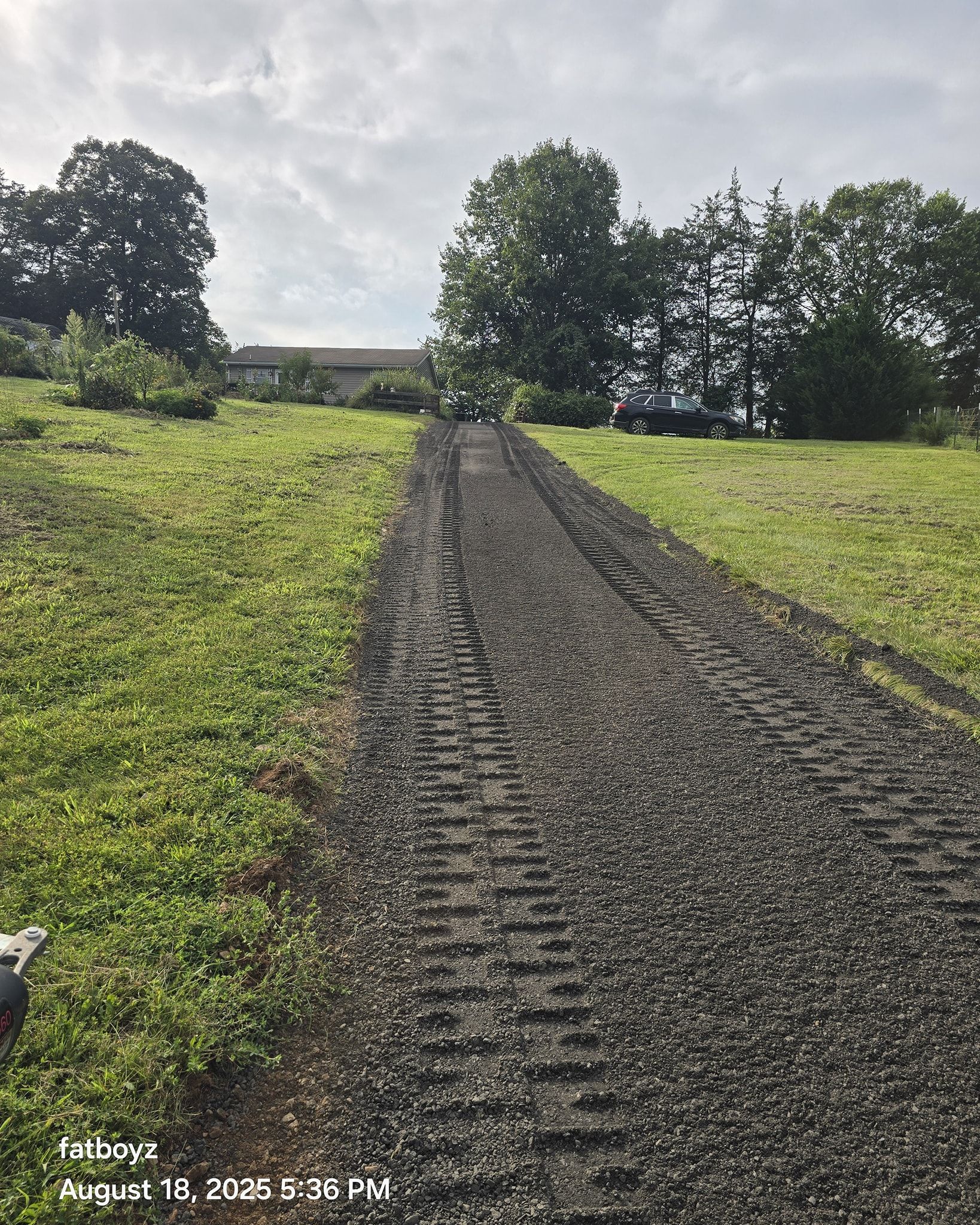 Gravel path leading through a green field toward trees under a cloudy sky