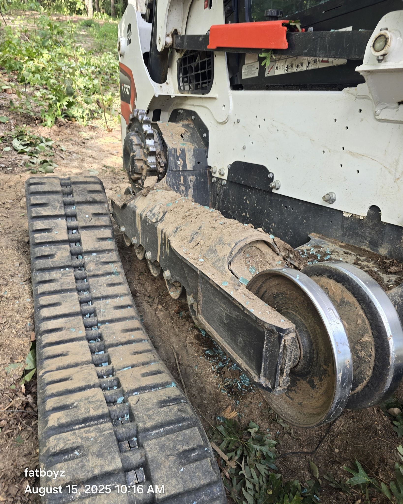 Close-up of a muddy tracked construction vehicle on a dirt path in a wooded area