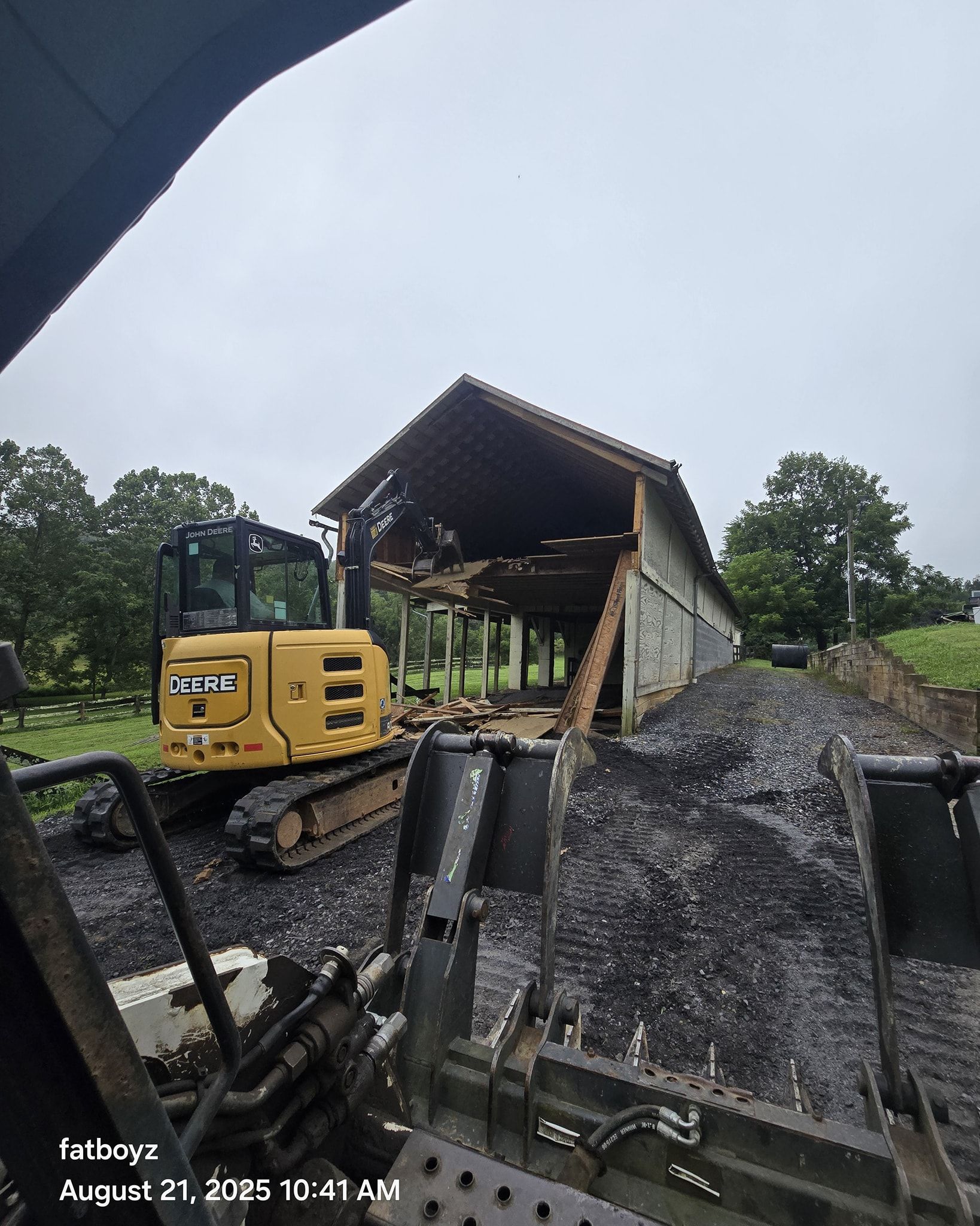Yellow excavator at a gravel quarry under a large wooden shelter.