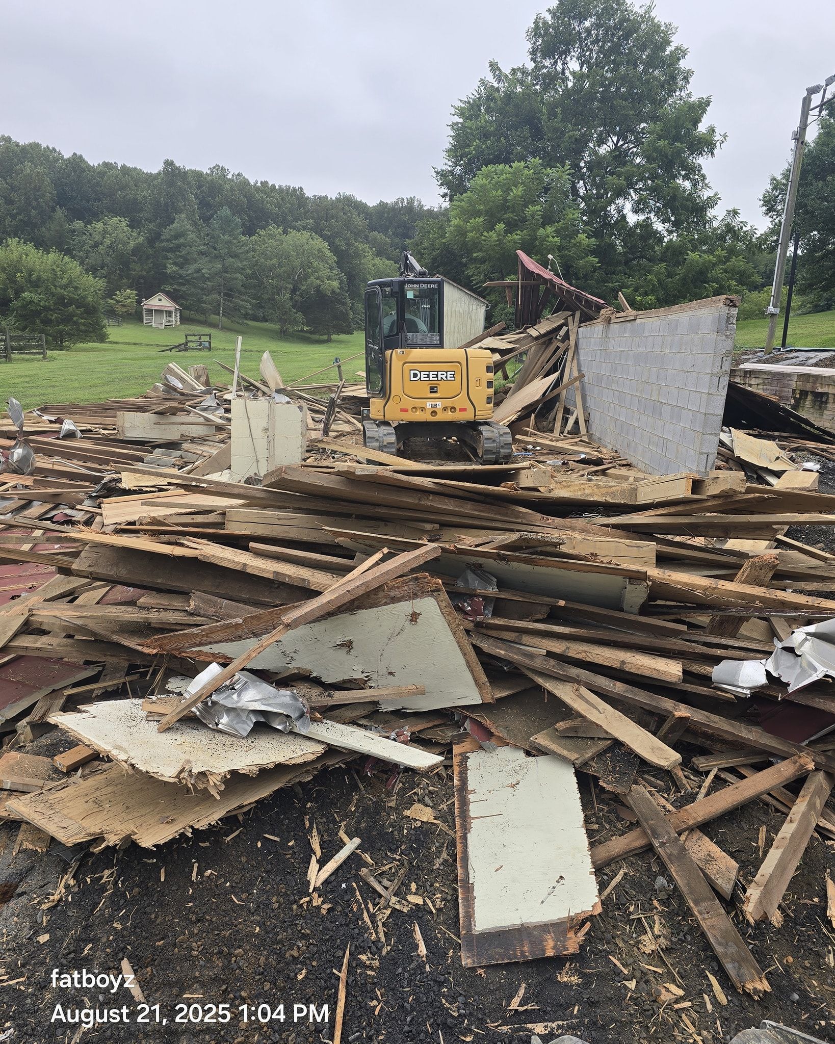 Yellow excavator amid debris from a demolished building in a wooded area.