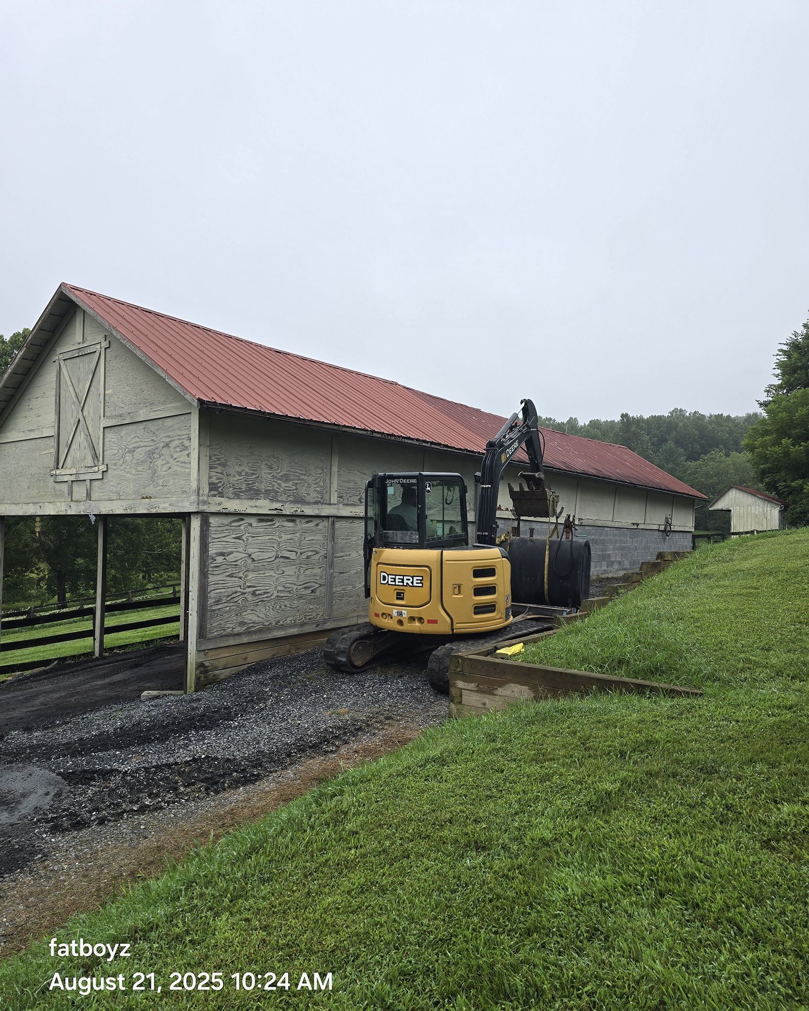 Yellow excavator beside a long stone building with a red roof on a muddy path