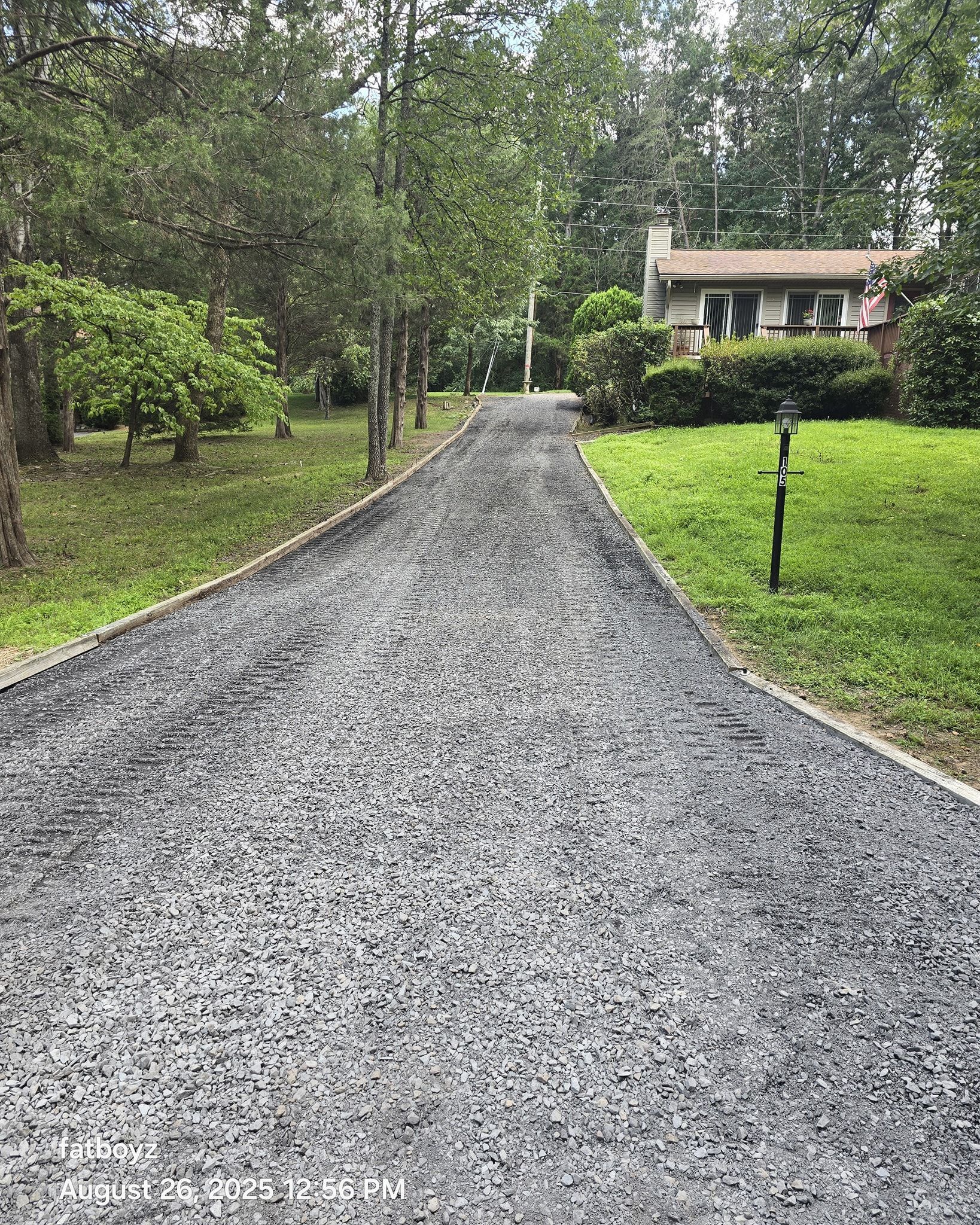 Gravel driveway leading to a house surrounded by trees and green lawn.