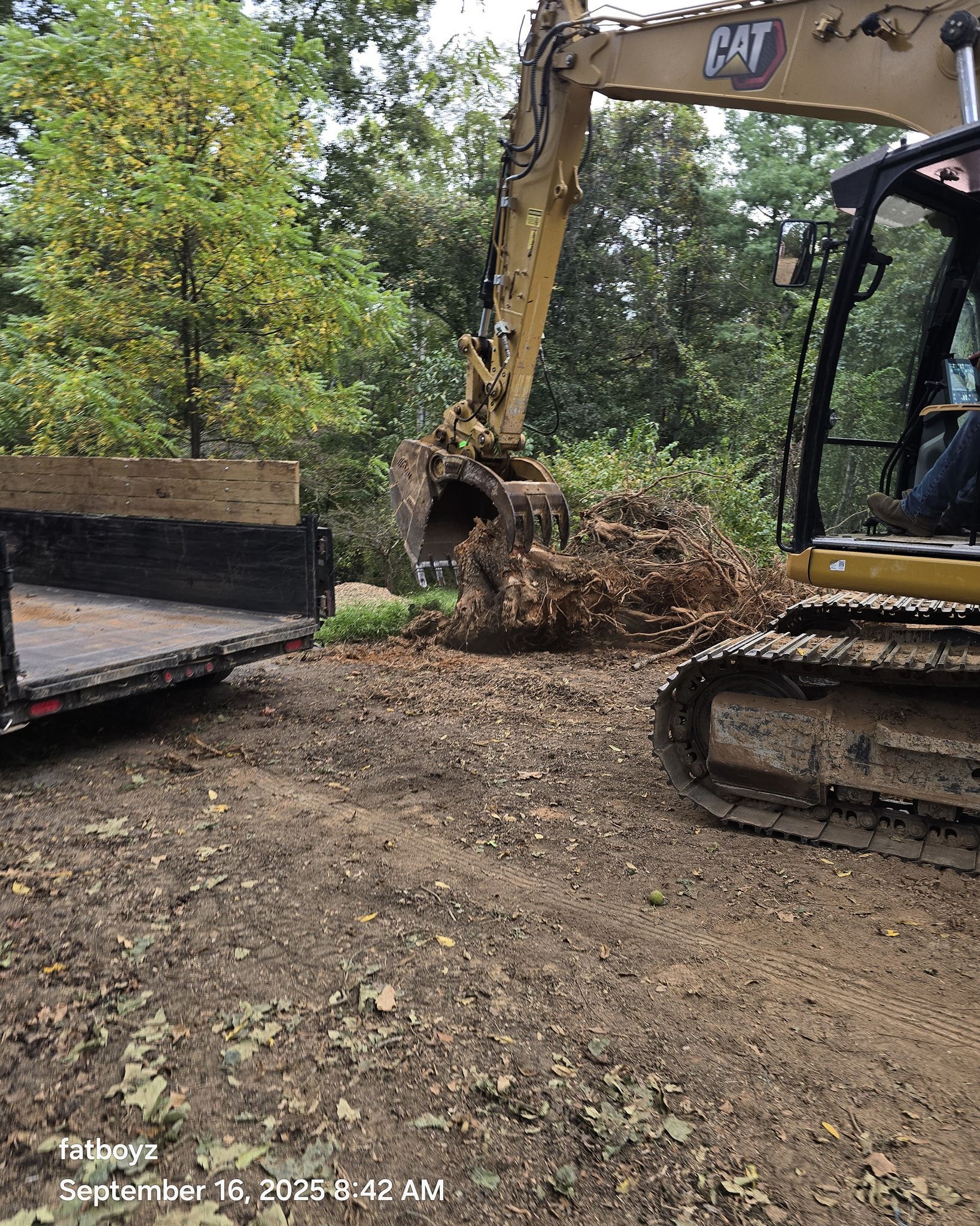 Excavator loading dirt and roots into a truck at a muddy construction site
