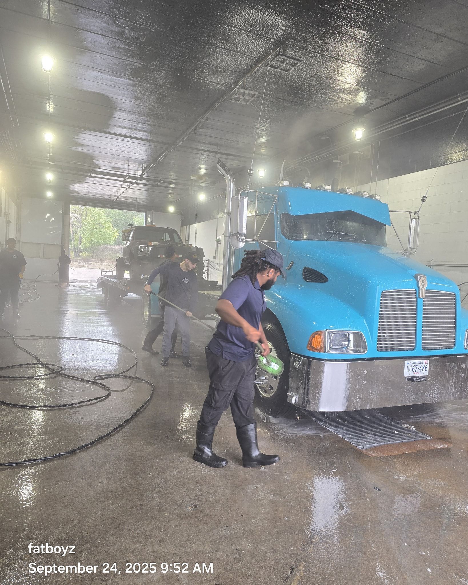 Workers washing a blue semi-truck inside a car wash tunnel