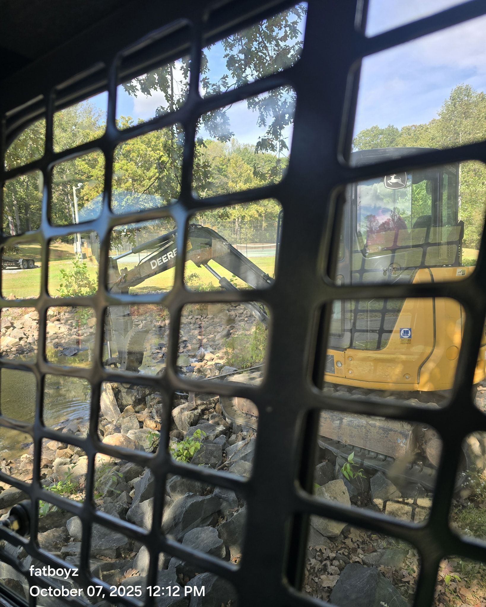 Yellow excavator seen through a window grid, clearing rubble at a demolition site.
