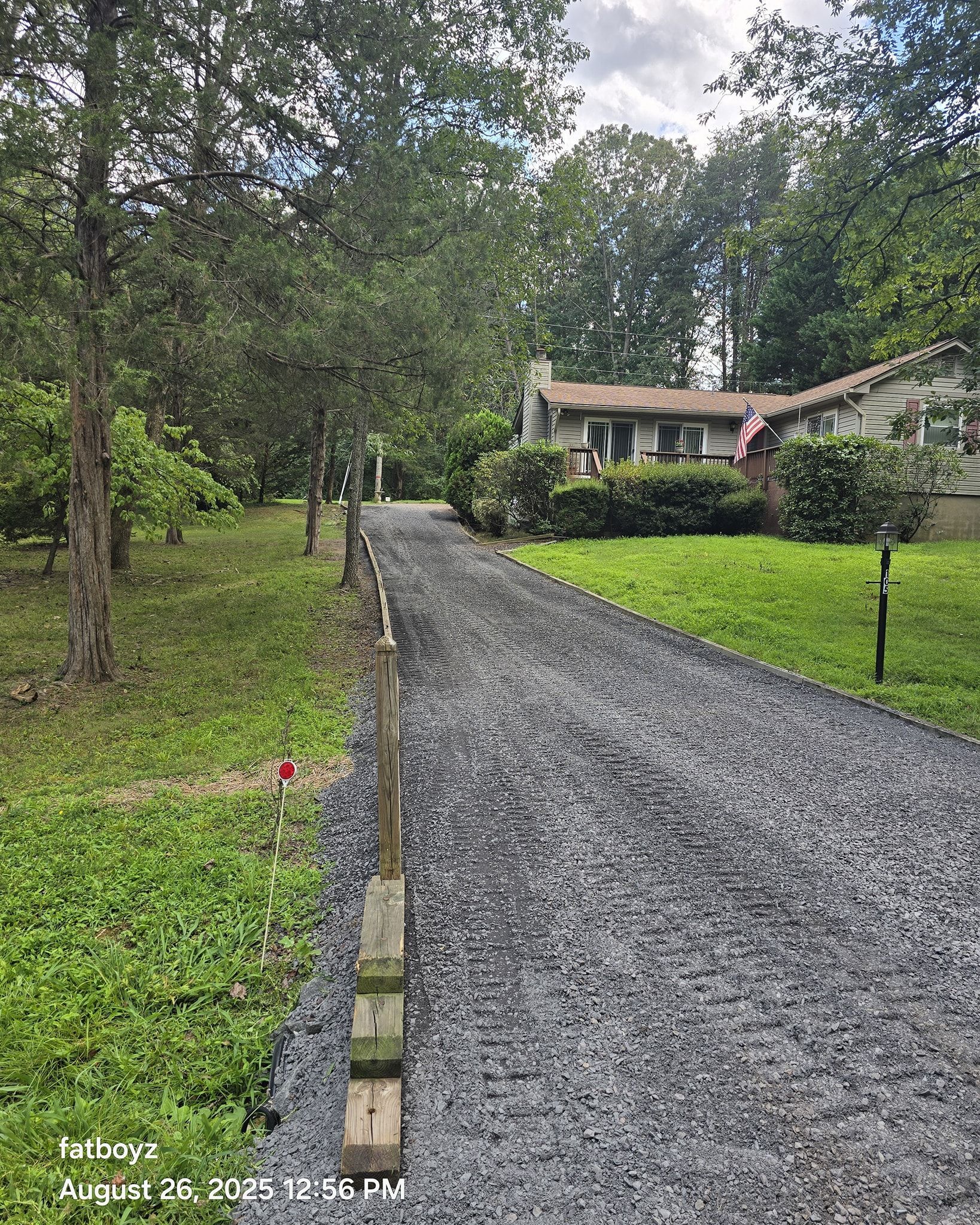 Gravel driveway leading to a house, bordered by grass and trees under an overcast sky