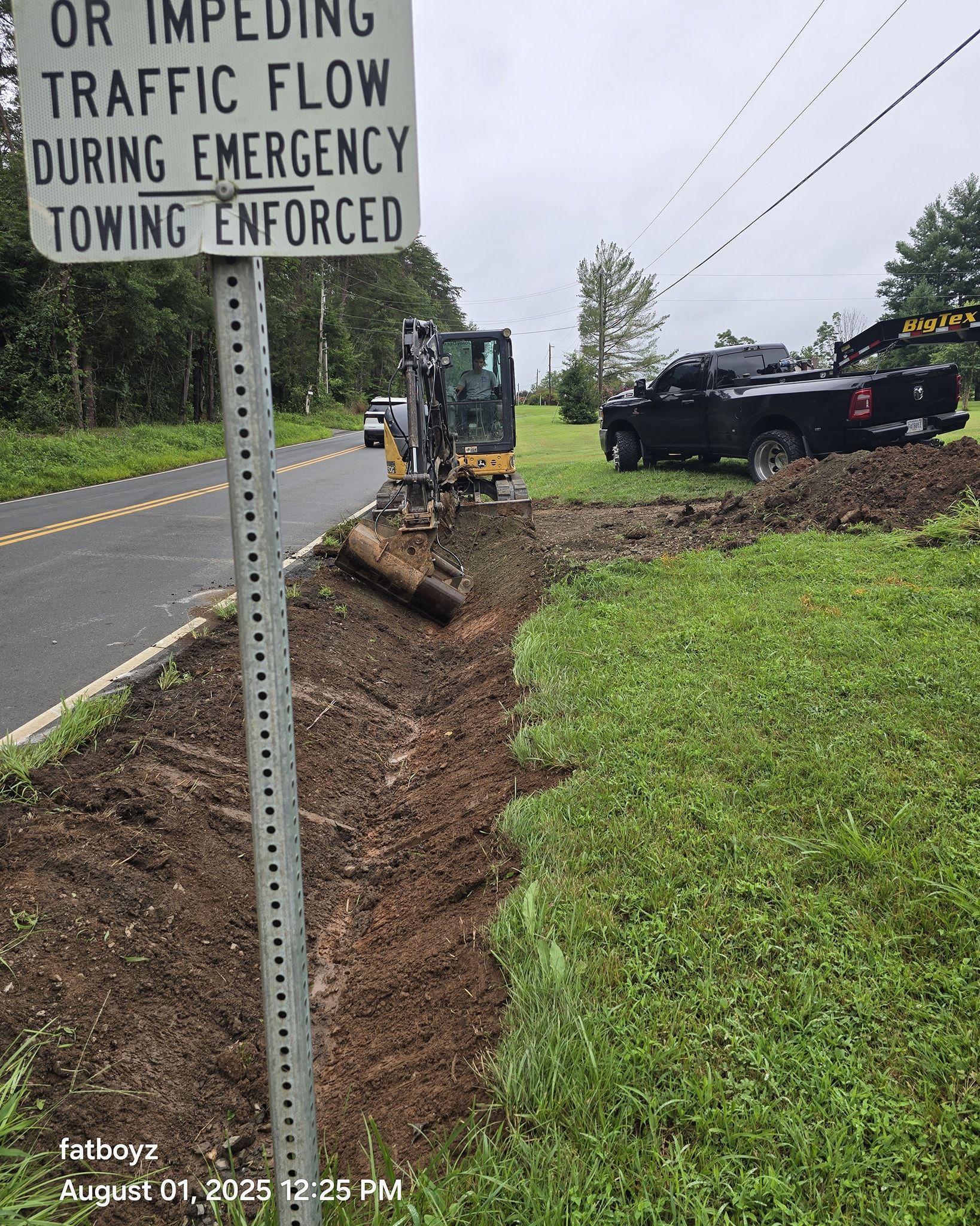 Roadside towing sign, muddy shoulder, and overturned black vehicle near a utility truck