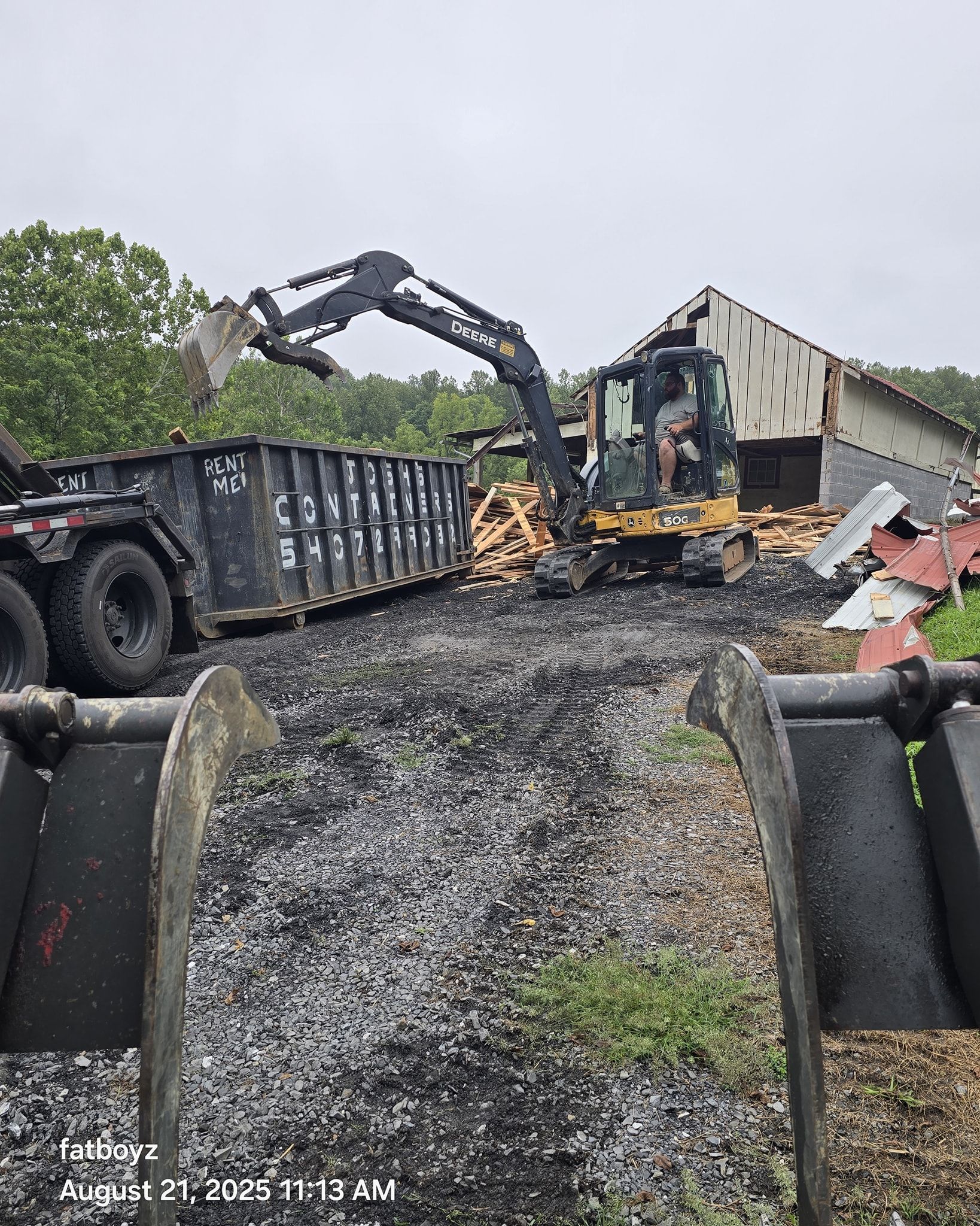 Dump truck and excavator on a muddy demolition site, with debris and charred ground.
