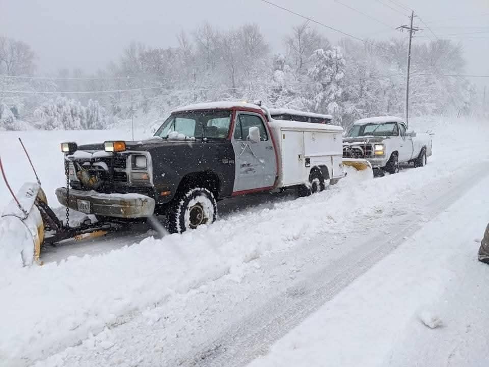 Snowplow truck and pickup stuck in deep snow on a snowy roadside.