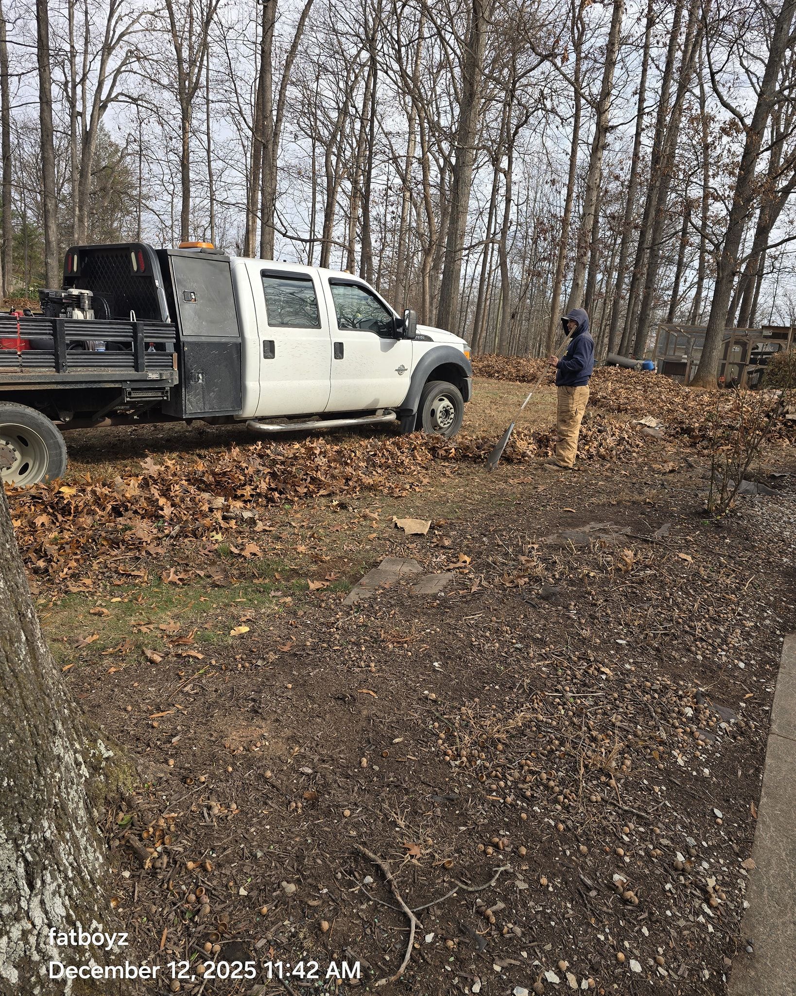 White pickup truck on a leaf-covered dirt road in a wooded area, with a person standing nearby.