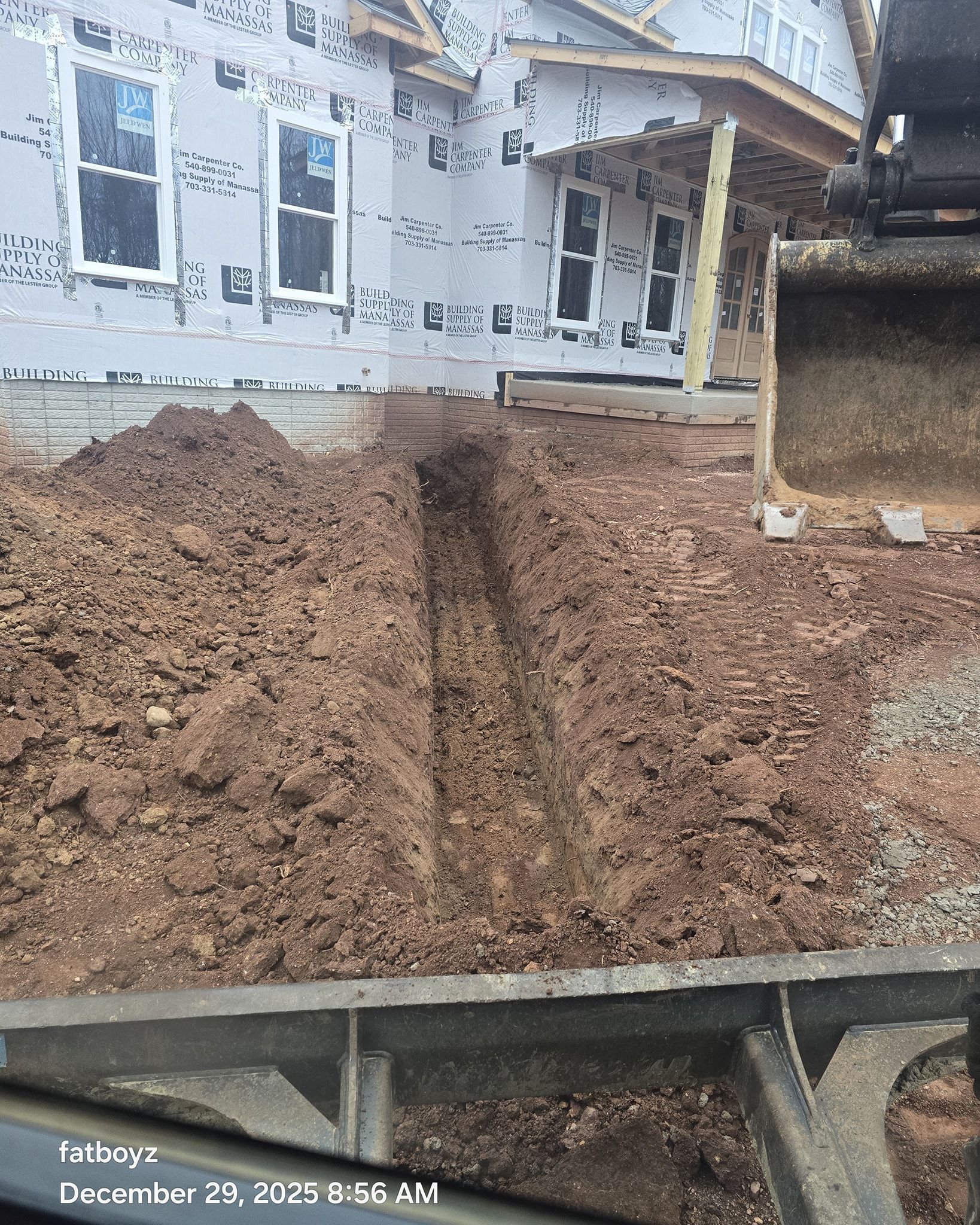 Freshly piled dirt in front of a house under construction, with a concrete border in the foreground.