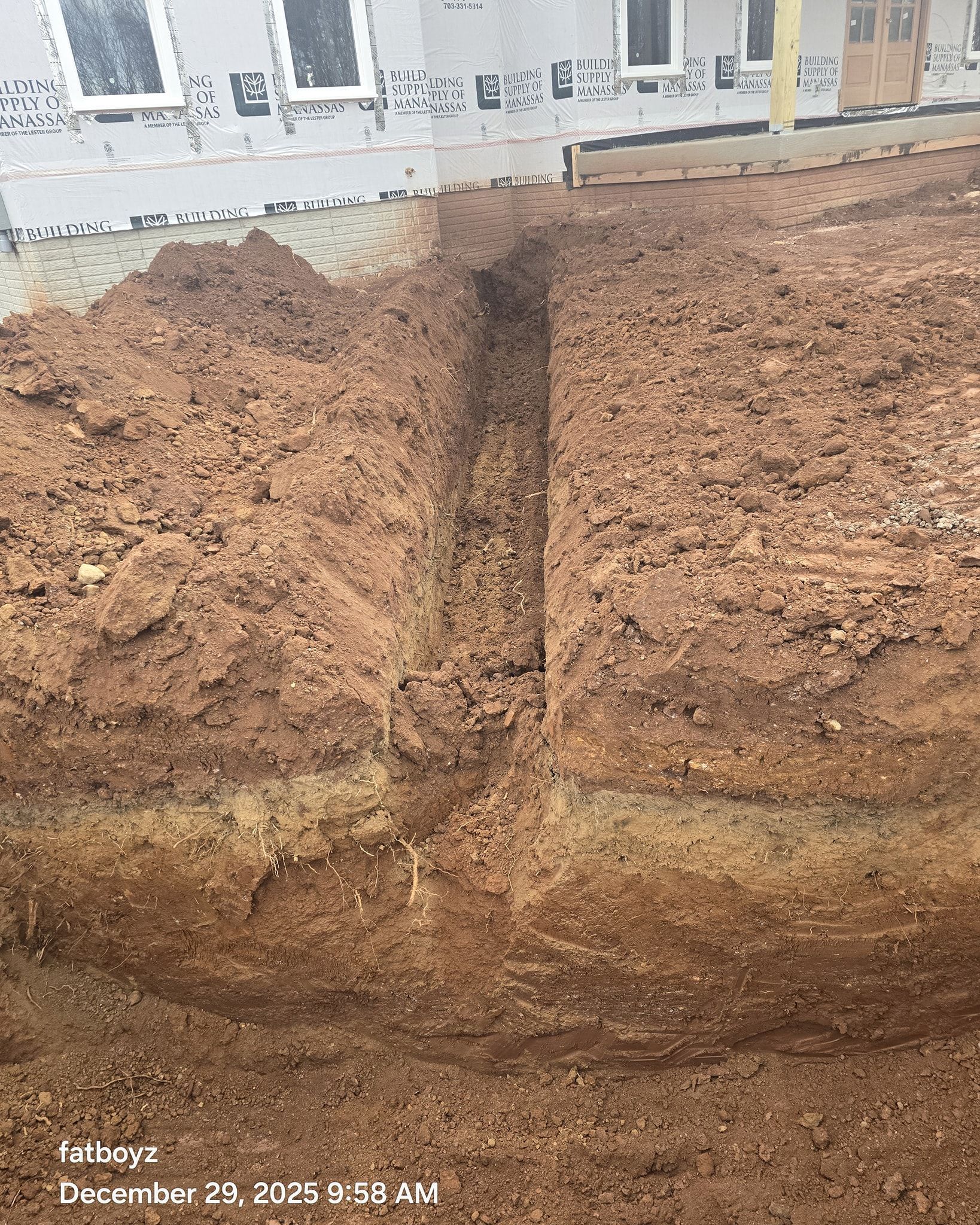 Close-up of a muddy earthen wall with a dark vertical crack below building windows.